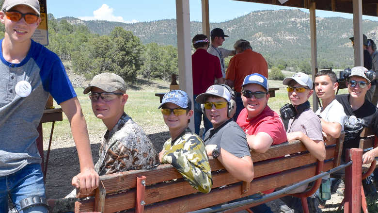 Group of young people sitting on a bench at a gun range in the mountains.