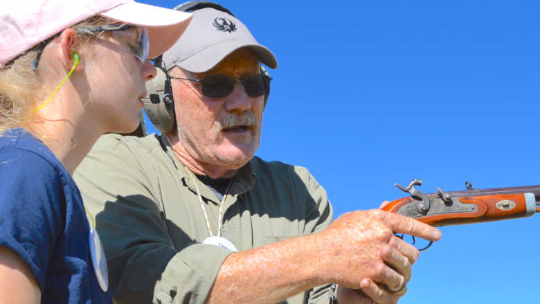 Seasoned instructor showing a young person how to shoot a flintlock pistol