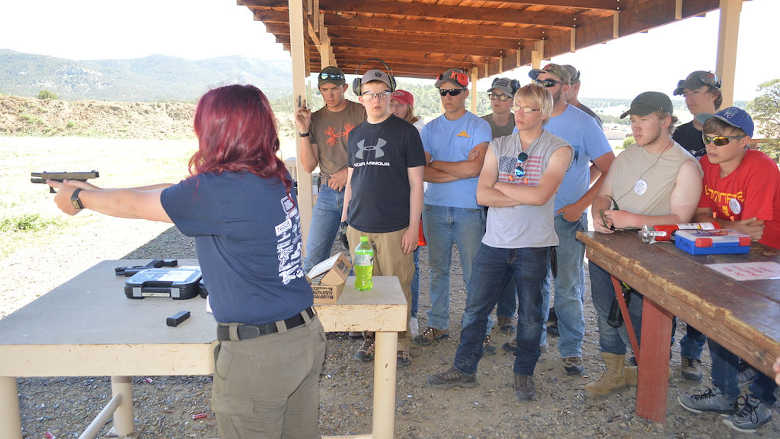 A firearm instructor displays the proper way to shoot a firearm to a group of young people.