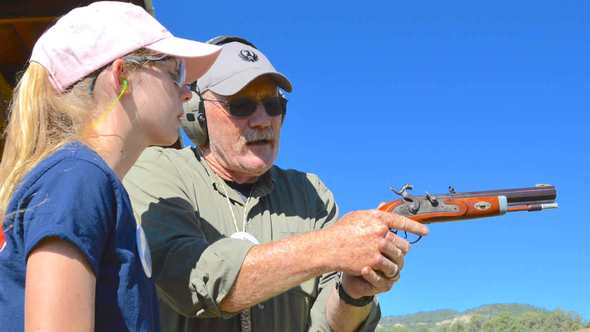 Expert instructor shows a girl in a pink hat how to properly handle a musket pistol at the NRA Whittington Center 